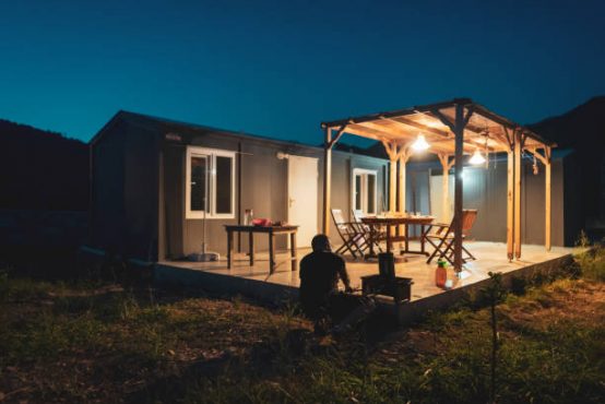 Mature man preparing barbecue dinner in backyard of container house.